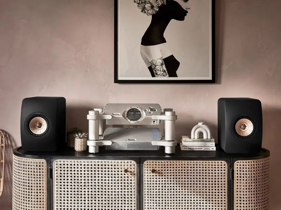 DAVE in a silver Choral Ensemble stand on a cane sideboard, between a pair of black bookshelf loudspeakers