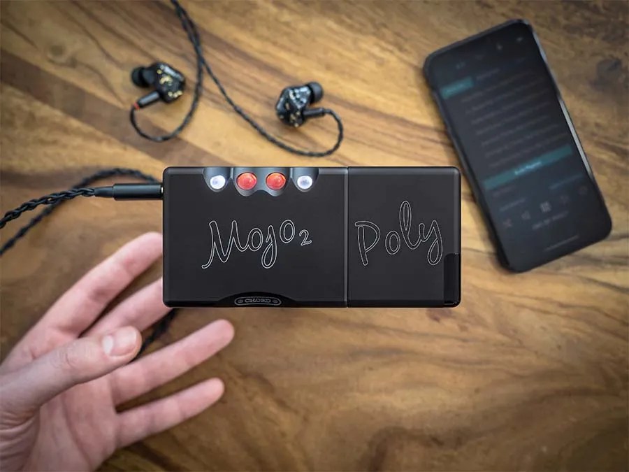 The Mojo 2 and Poly pair on a wooden table with a cabled pair of in-ear monitors and a smartphone running a player app